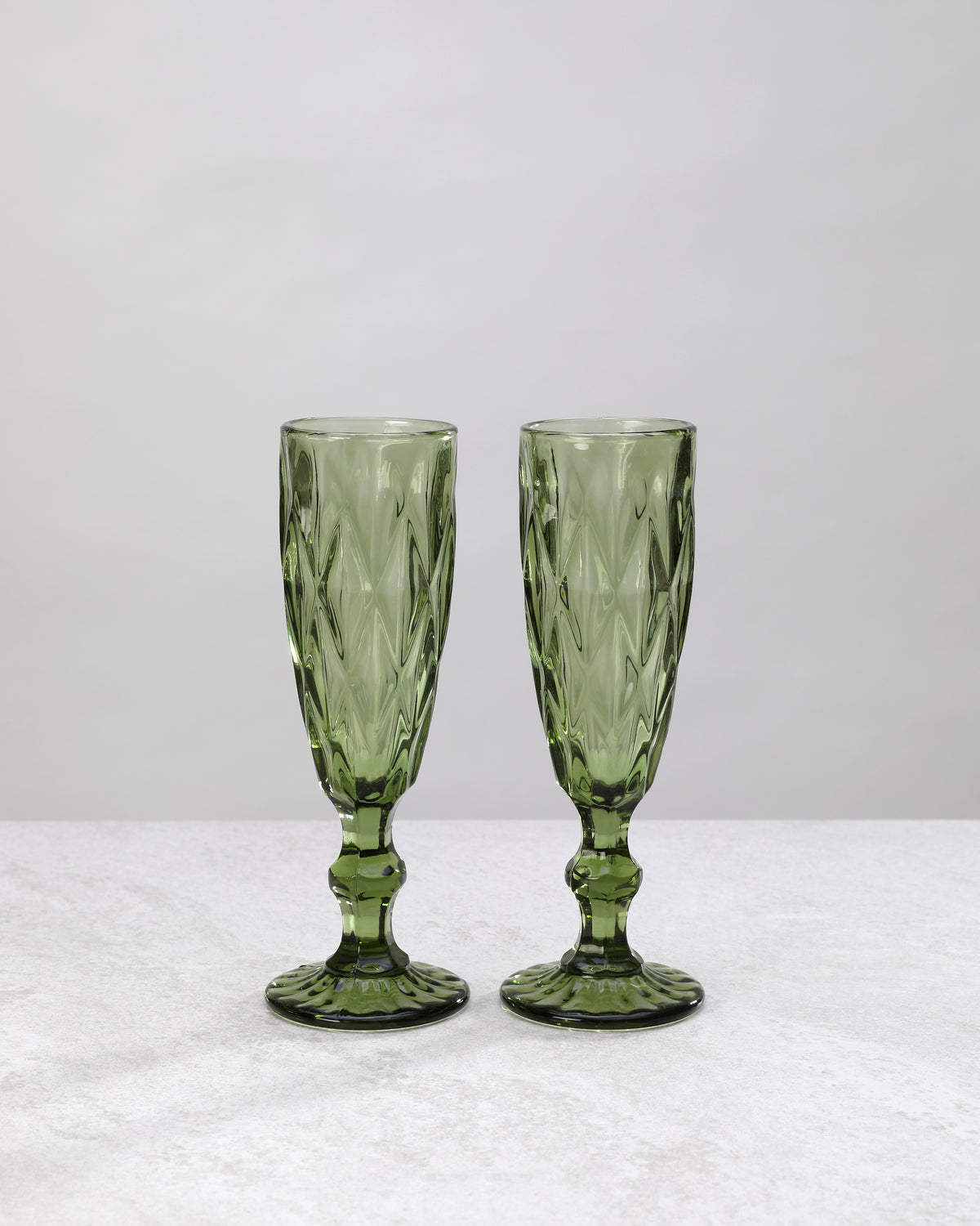 Two olive green diamond cut champagne flutes, on white