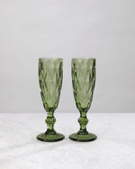 Two olive green diamond cut champagne flutes, on white