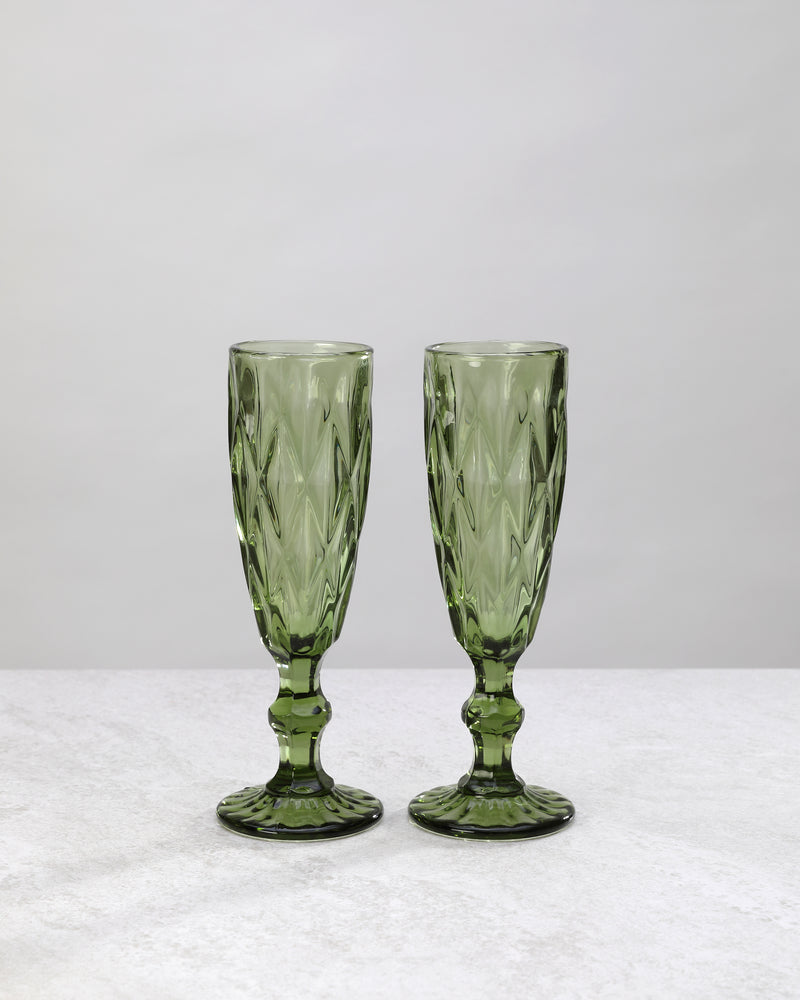 Two olive green diamond cut champagne flutes, on white