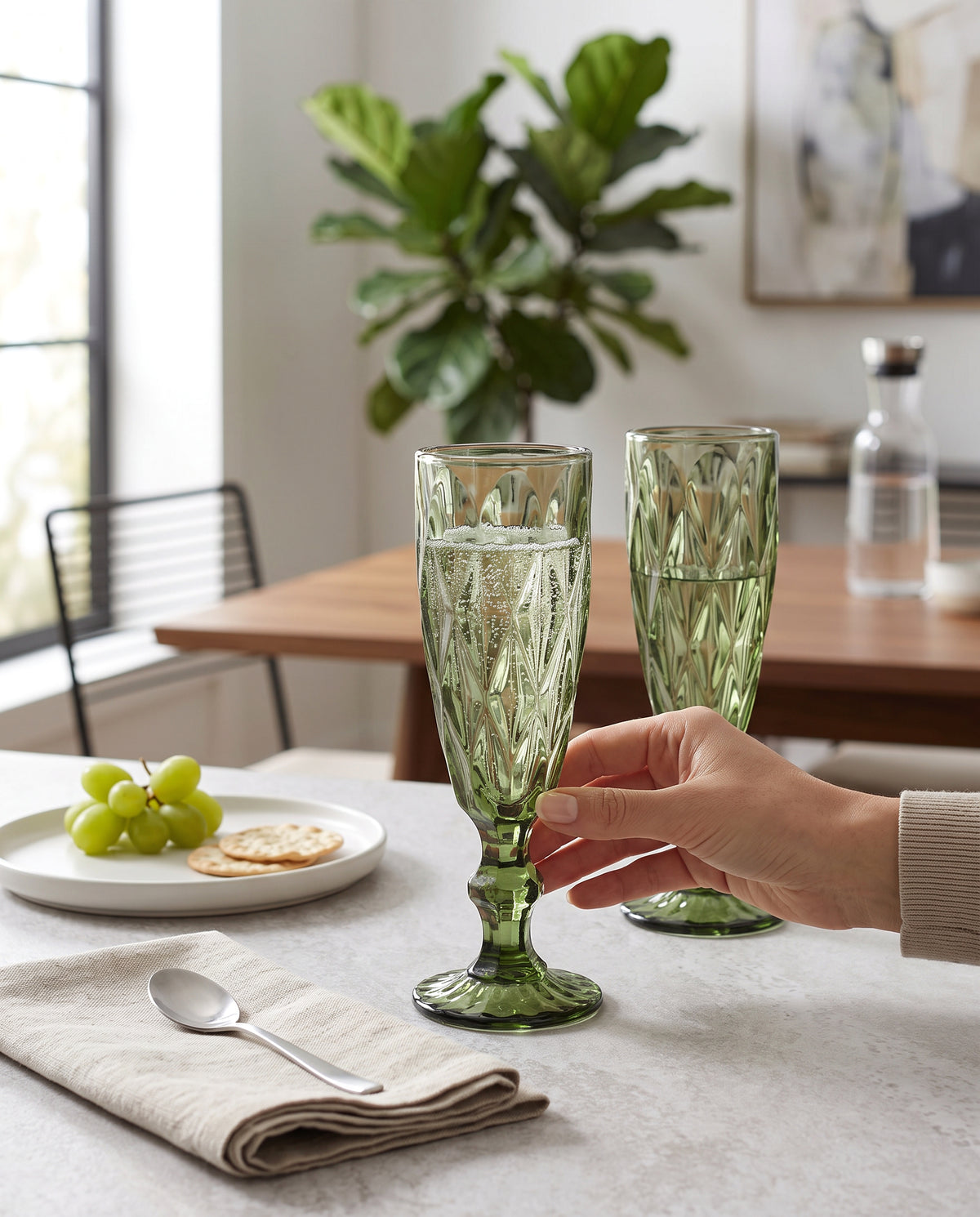 Olive diamond cut champagne flutes being raised at a table set with grapes