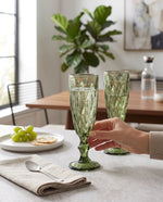 Olive diamond cut champagne flutes being raised at a table set with grapes