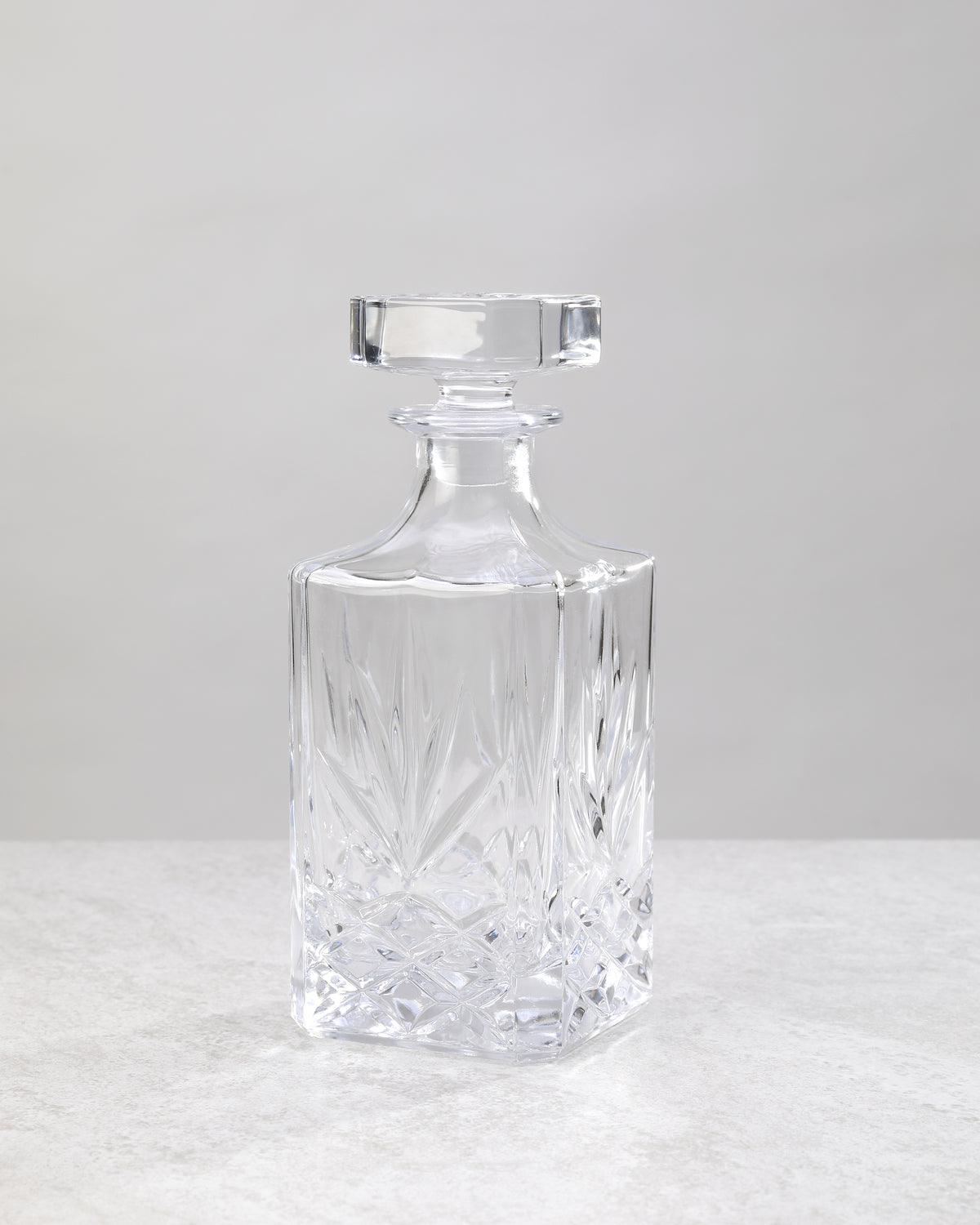 Clear machine cut glass decanter with a square stopper, on white