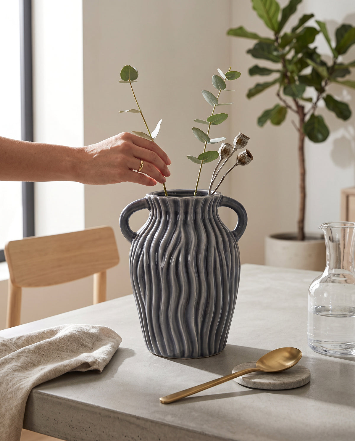 Hand placing the grey ribbed ceramic pot on a table beside greenery