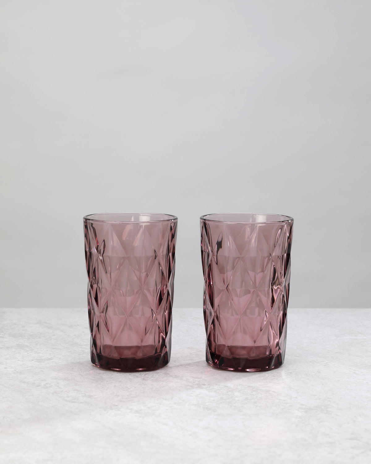 Two tall pink diamond cut highball glasses, on white