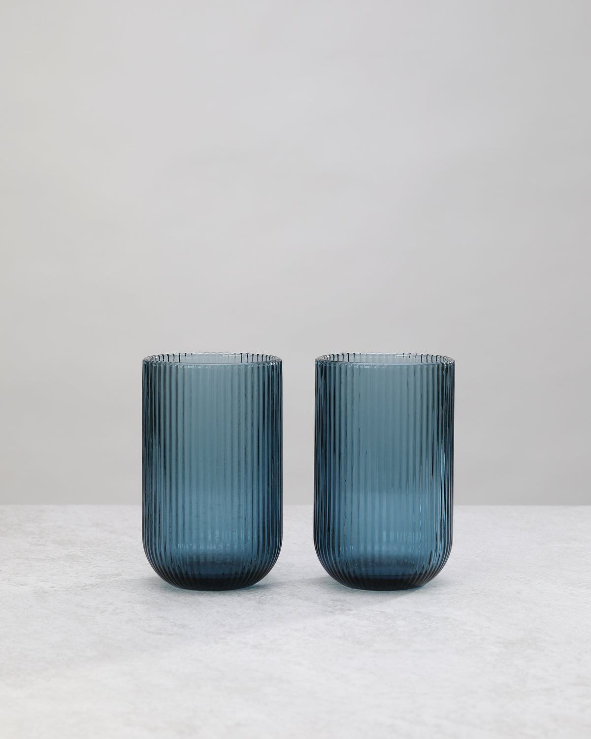 Two tall blue ribbed highball glasses side by side, on white