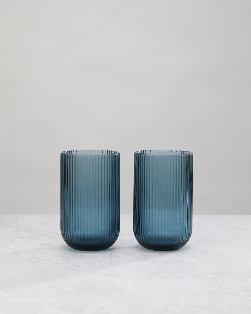 Two tall blue ribbed highball glasses side by side, on white