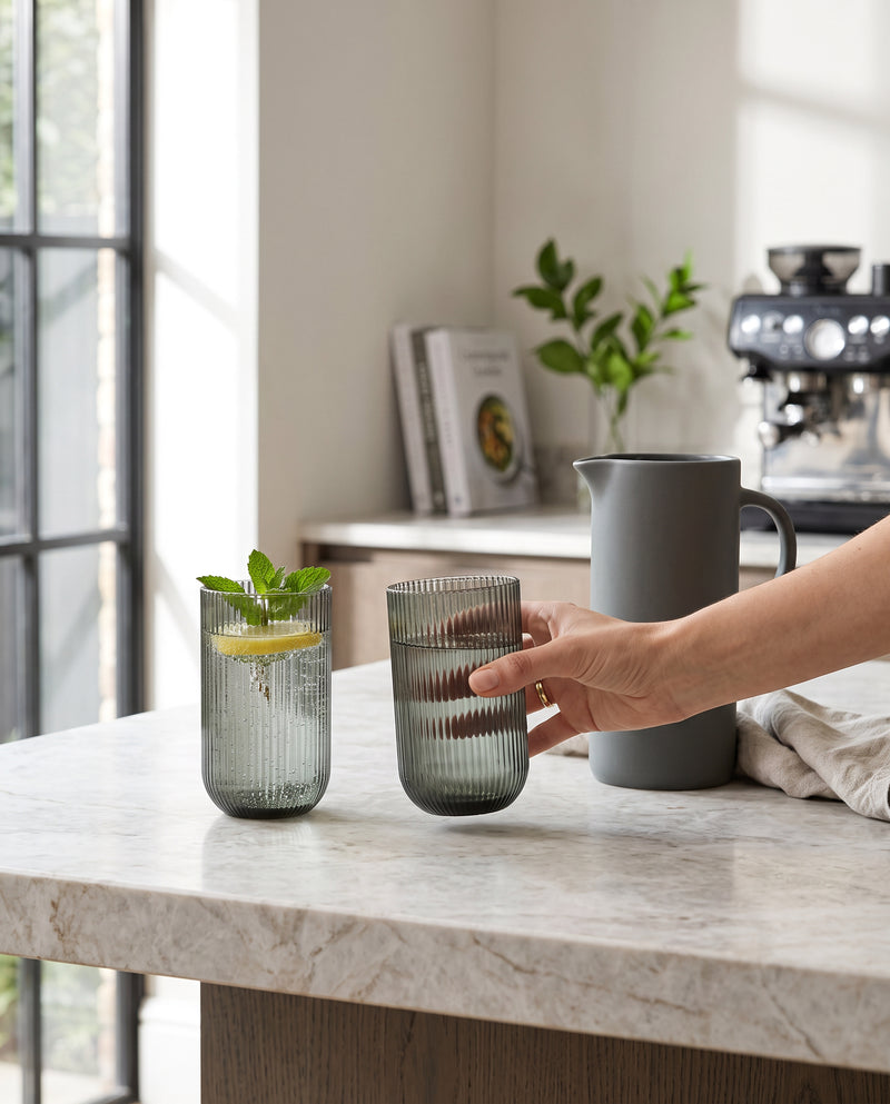 Hunter green ribbed highball glasses with mint on a kitchen counter, a hand picking one up