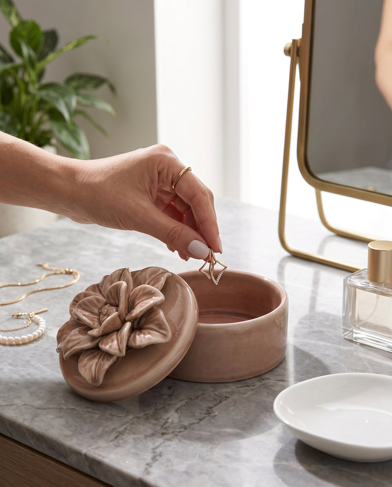 Hand placing jewellery in the pink glazed ceramic trinket box on a dresser
