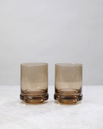 Two smoky coffee-brown tumbler glasses with a thick base, on white