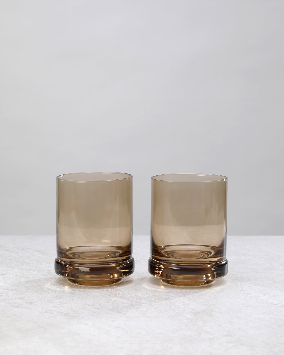 Two smoky coffee-brown tumbler glasses with a thick base, on white