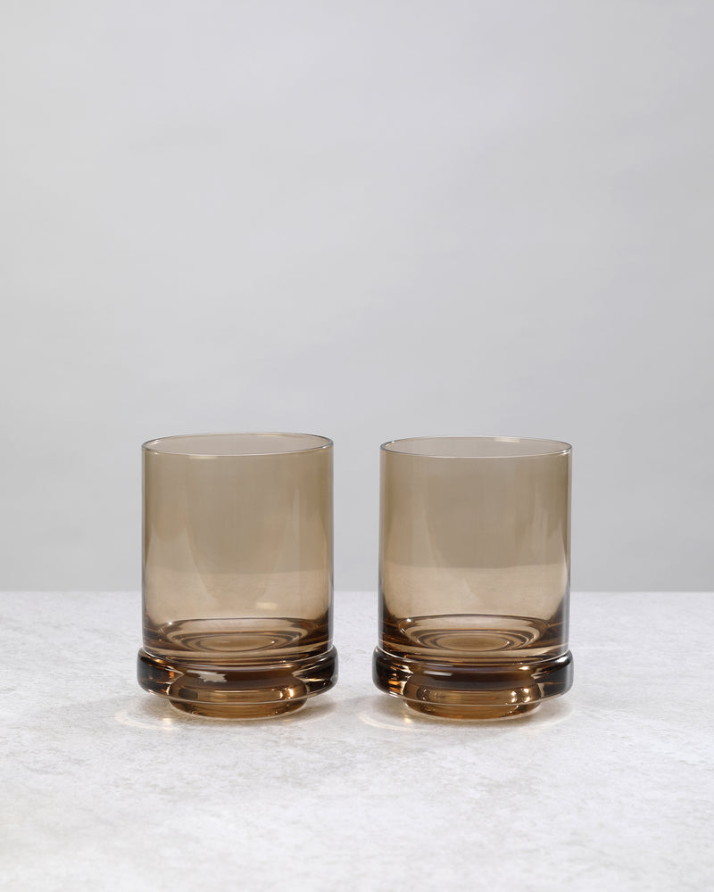 Two smoky coffee-brown tumbler glasses with a thick base, on white