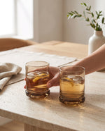 Coffee-brown tumblers with iced drinks on a stone table, a hand holding one