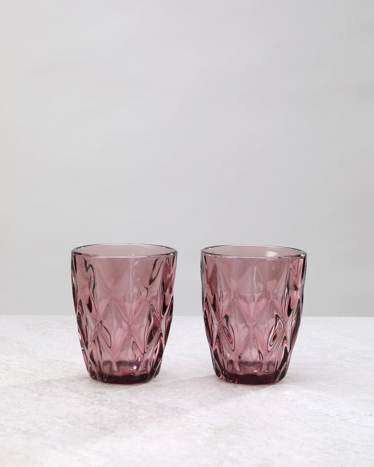 Two pink diamond cut tumbler glasses with a large faceted pattern, on white