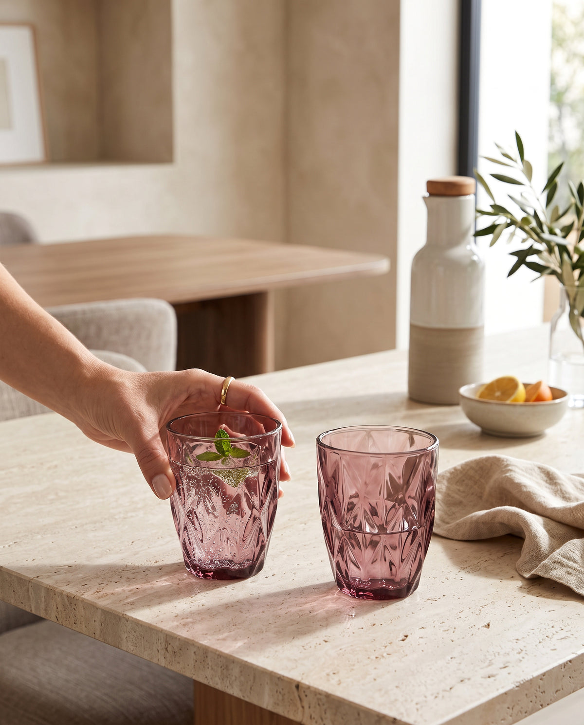 Pink diamond cut tumblers with mint drinks on a stone table, a hand lifting one