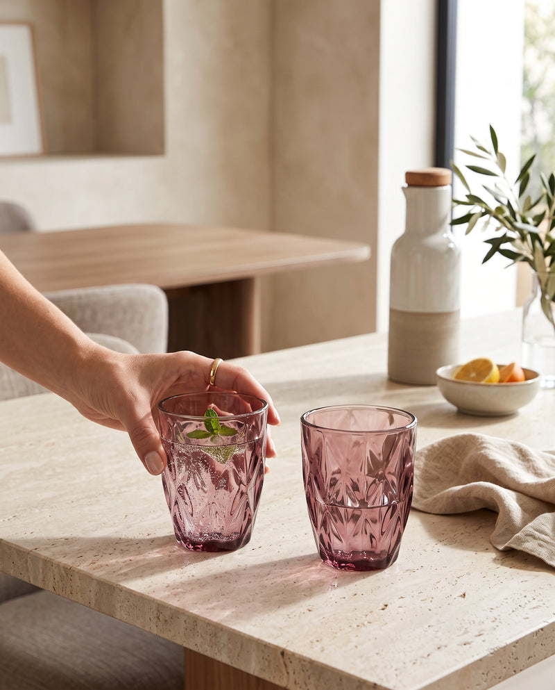 Pink diamond cut tumblers with mint drinks on a stone table, a hand lifting one