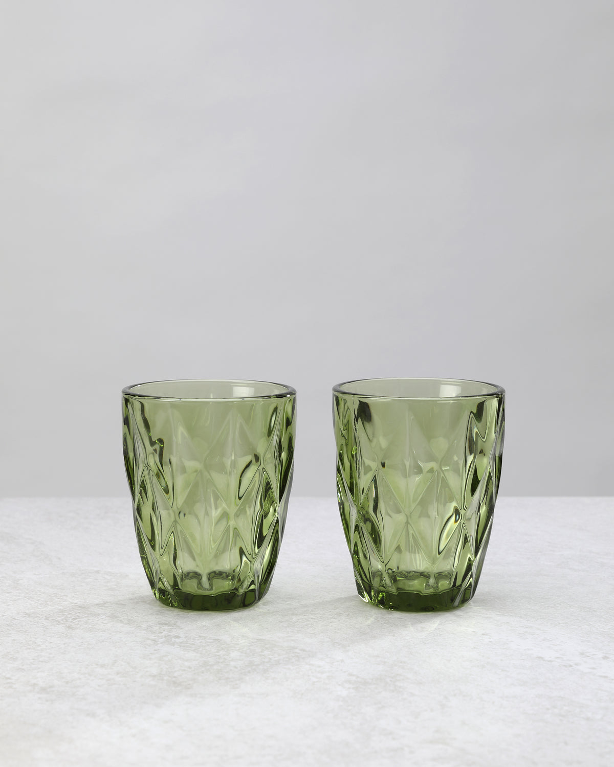 Two olive green diamond cut tumbler glasses with a large faceted pattern, on white