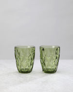 Two olive green diamond cut tumbler glasses with a large faceted pattern, on white