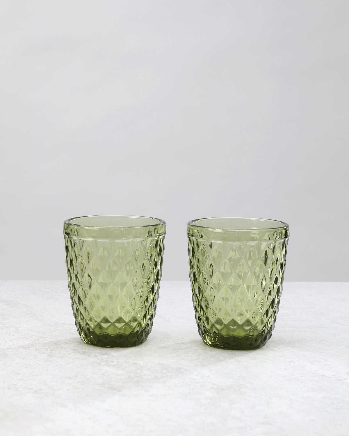 Two olive green small diamond tumbler glasses with an all-over diamond pattern, on white