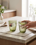 Olive green diamond tumblers with berries on a kitchen counter, a hand lifting one