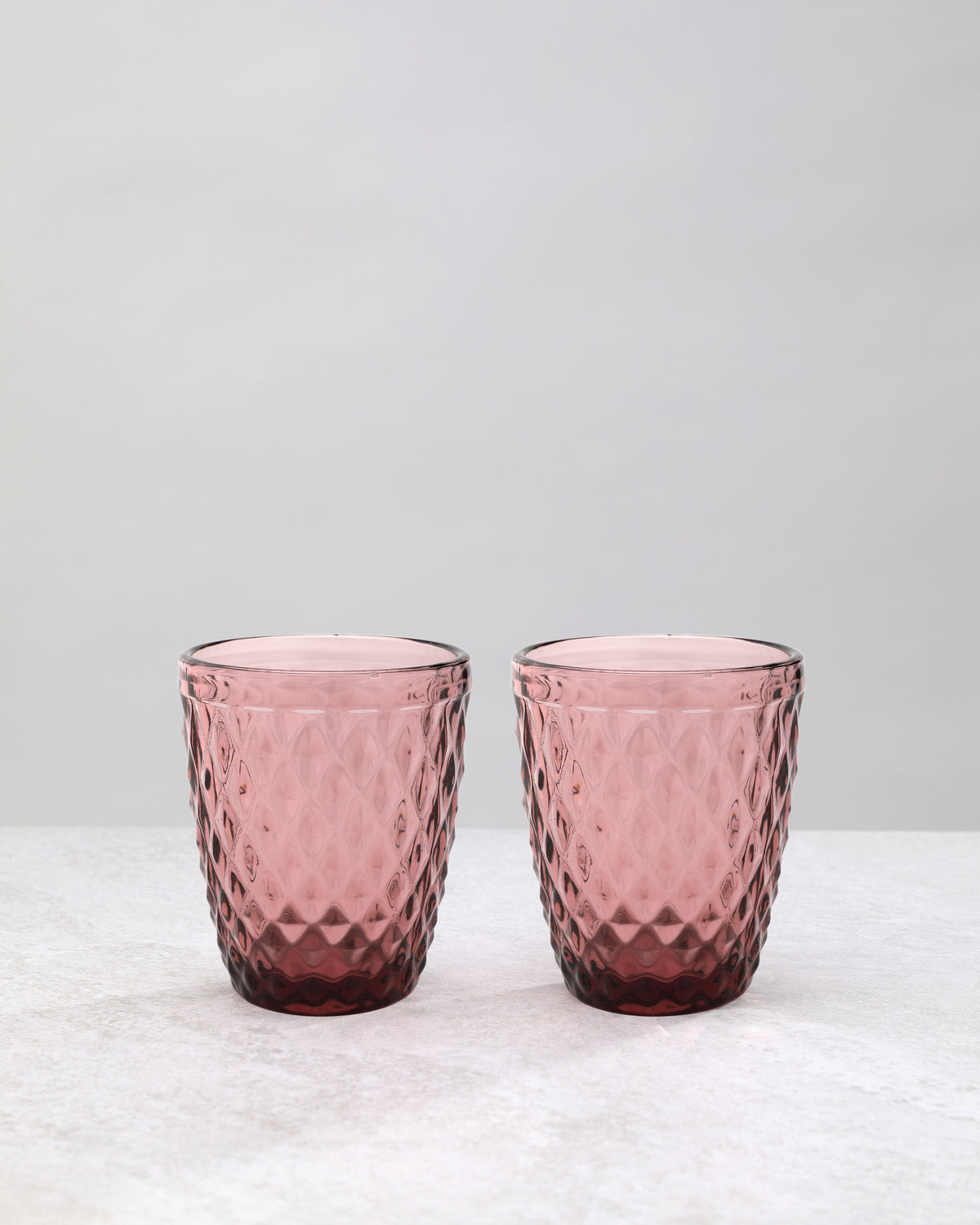 Pair of pink small diamond tumbler glasses on a white background