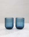 Two blue ribbed tumbler glasses side by side, on white