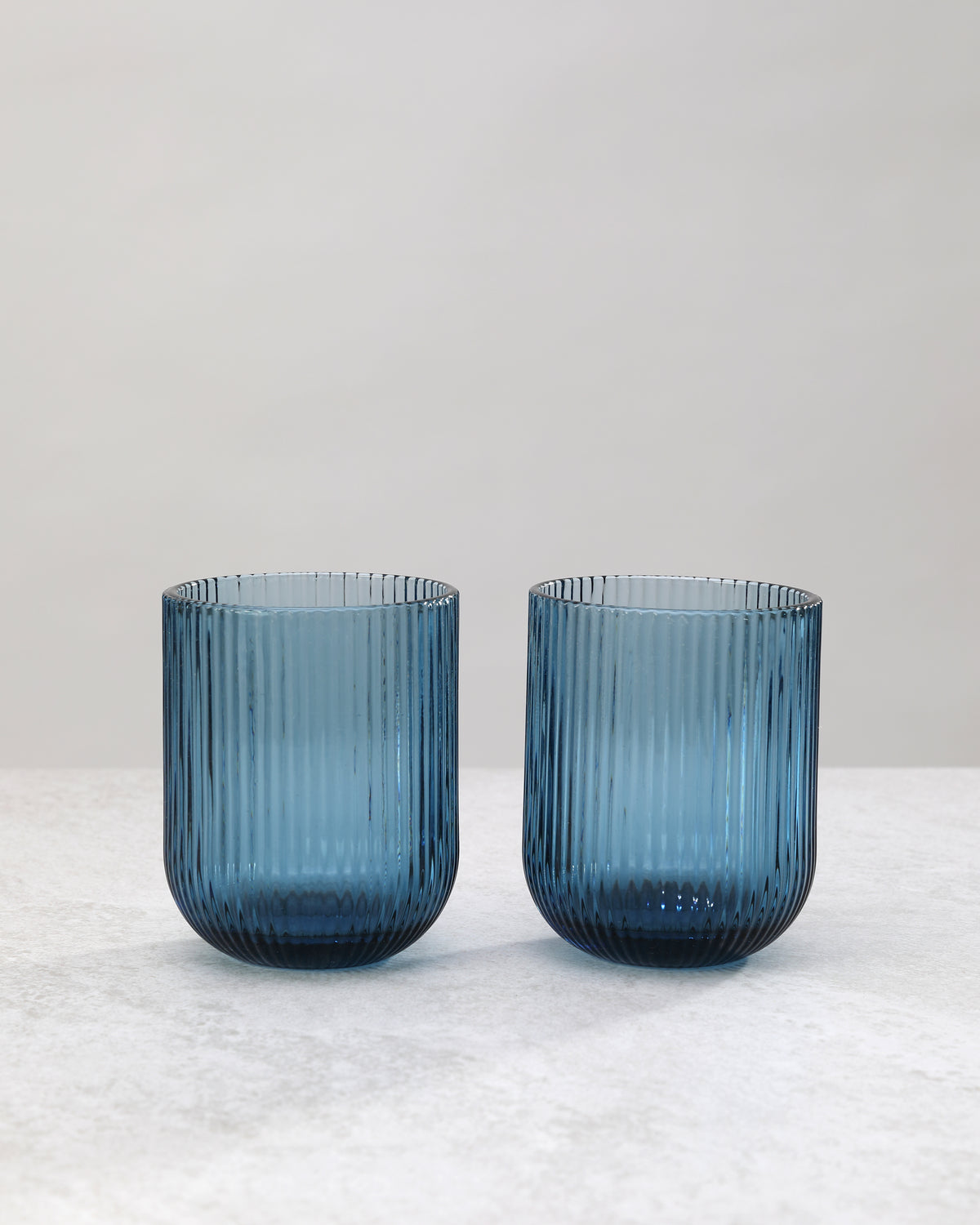 Two blue ribbed tumbler glasses side by side, on white