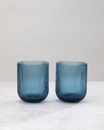 Two blue ribbed tumbler glasses side by side, on white