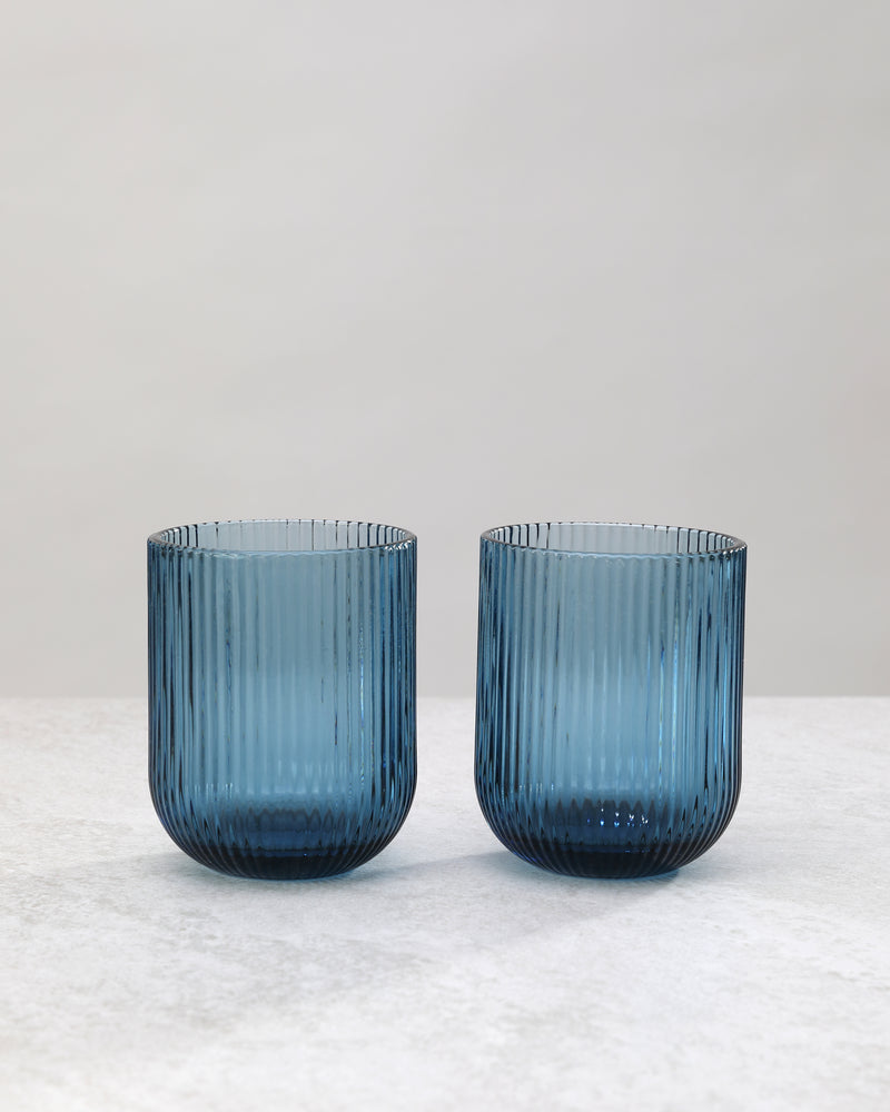 Two blue ribbed tumbler glasses side by side, on white