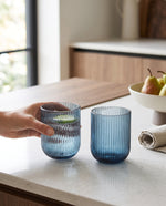 Blue ribbed tumblers on a kitchen counter beside a bowl of pears, a hand lifting one