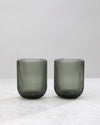 Two smoky hunter green ribbed tumbler glasses side by side, on white