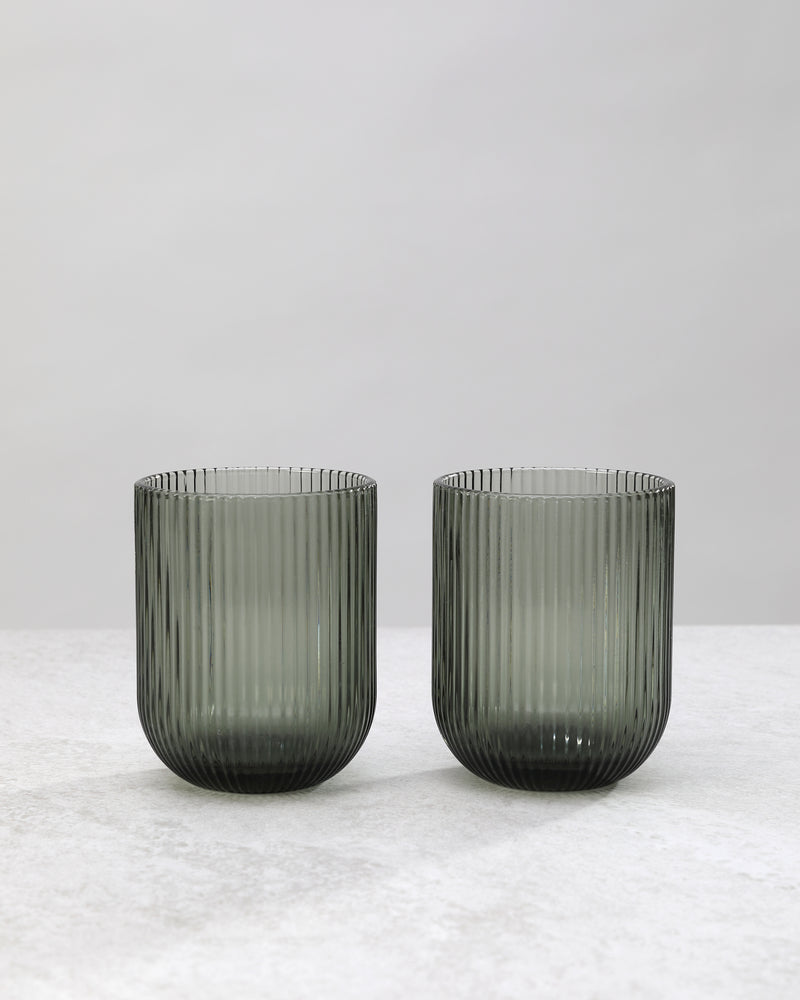 Two smoky hunter green ribbed tumbler glasses side by side, on white