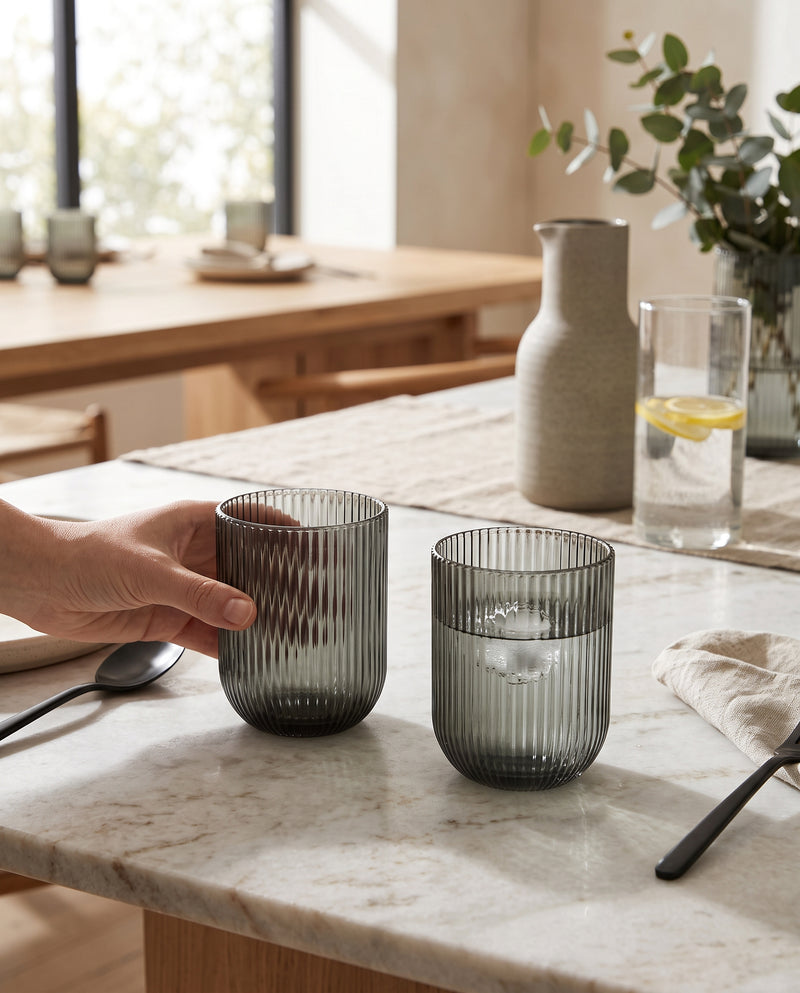 Hunter green ribbed tumblers on a kitchen counter, a hand lifting one filled with water