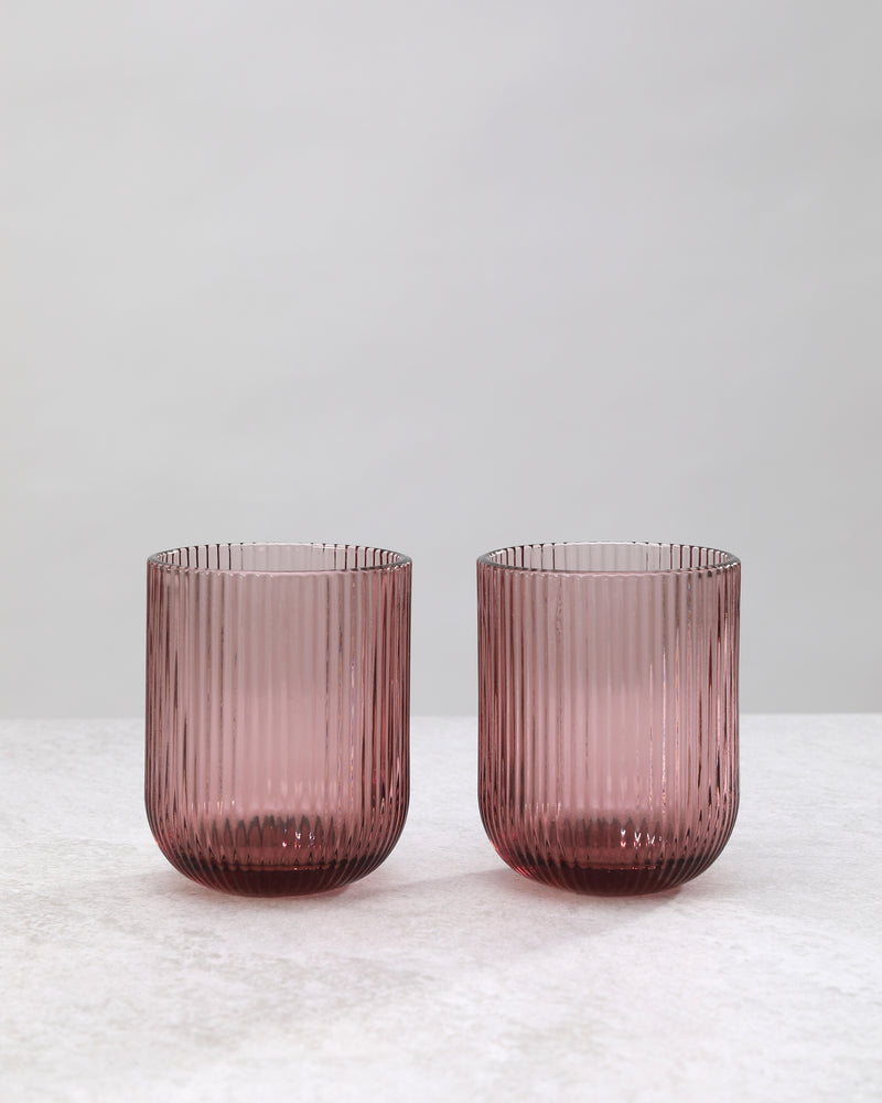 Two cordovan pink ribbed tumbler glasses side by side, on white