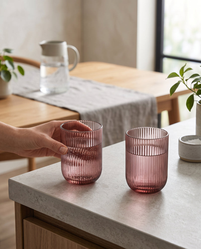 Cordovan ribbed tumblers on a kitchen counter, a hand lifting one, jug in the background