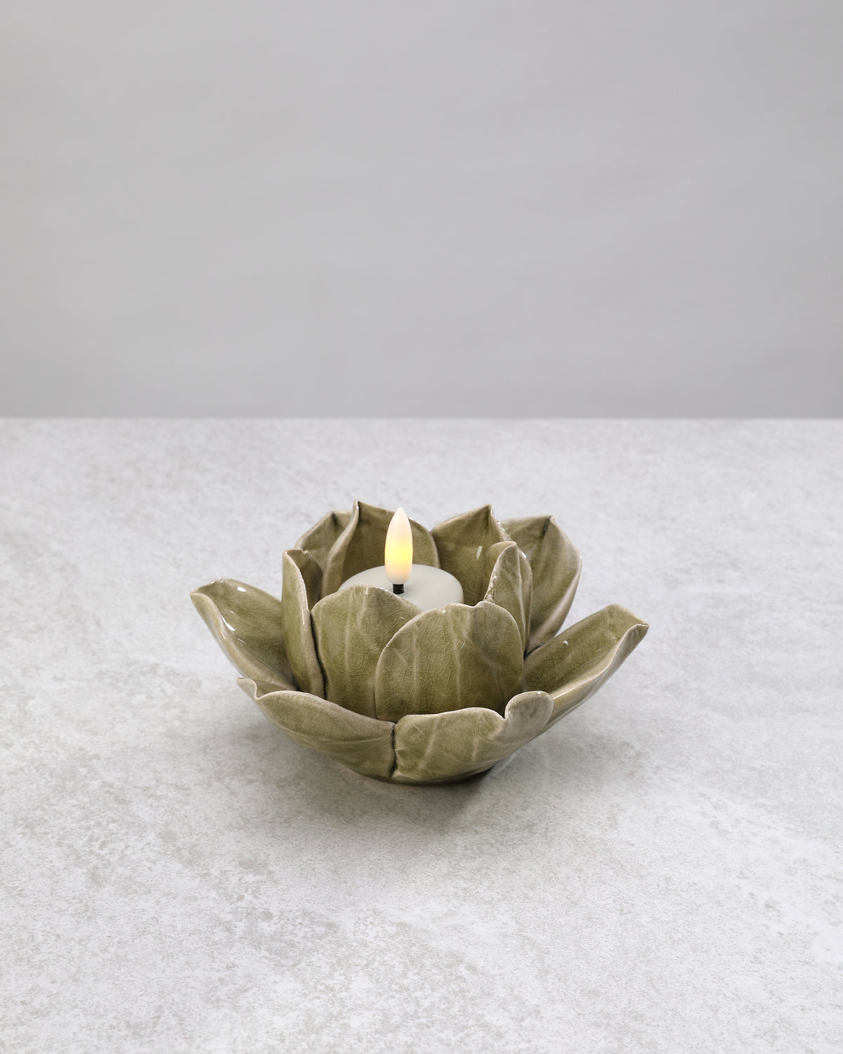 Sage green ceramic lotus tea light holder with a lit candle