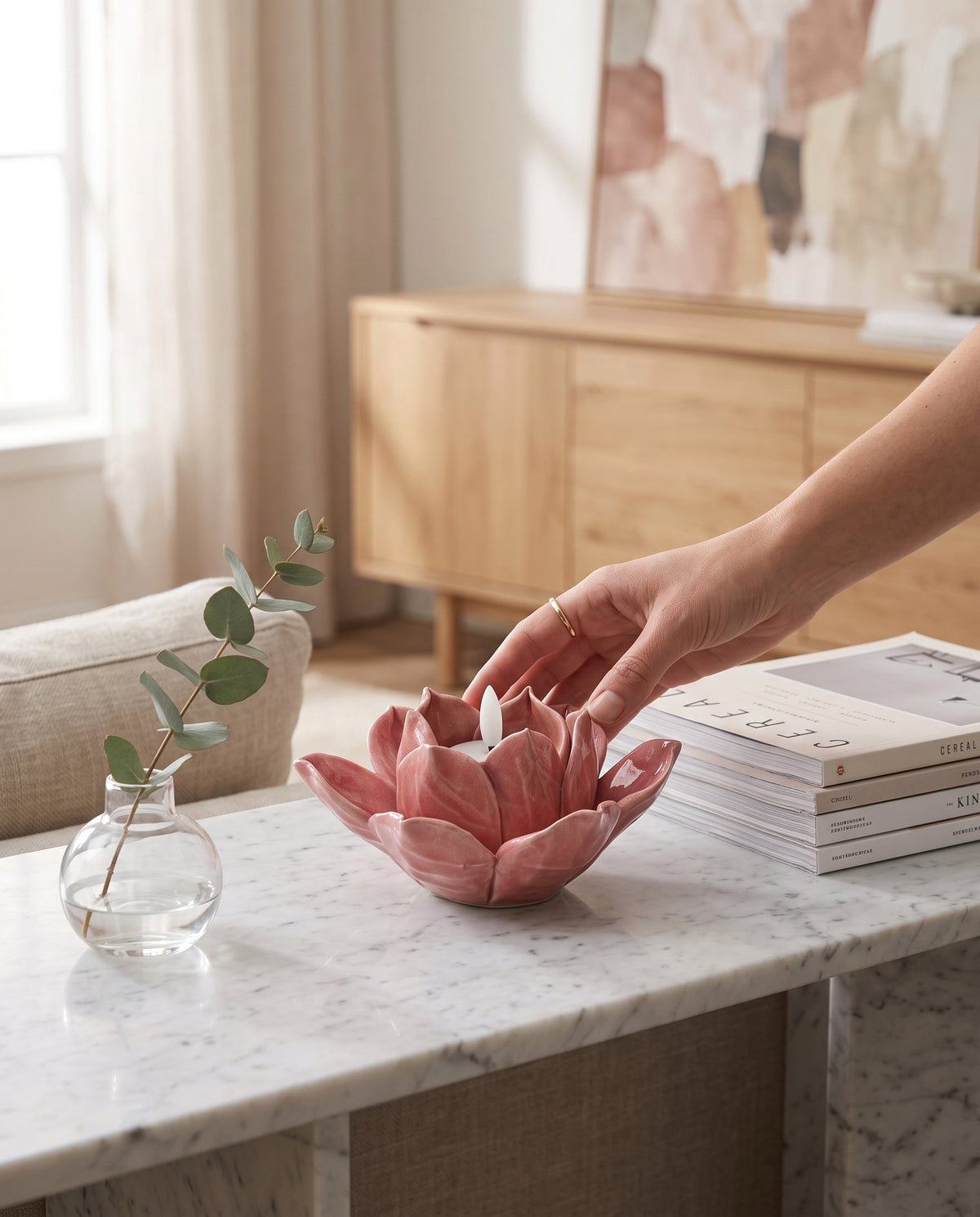 Hand placing a pink lotus tea light holder on a marble console beside books