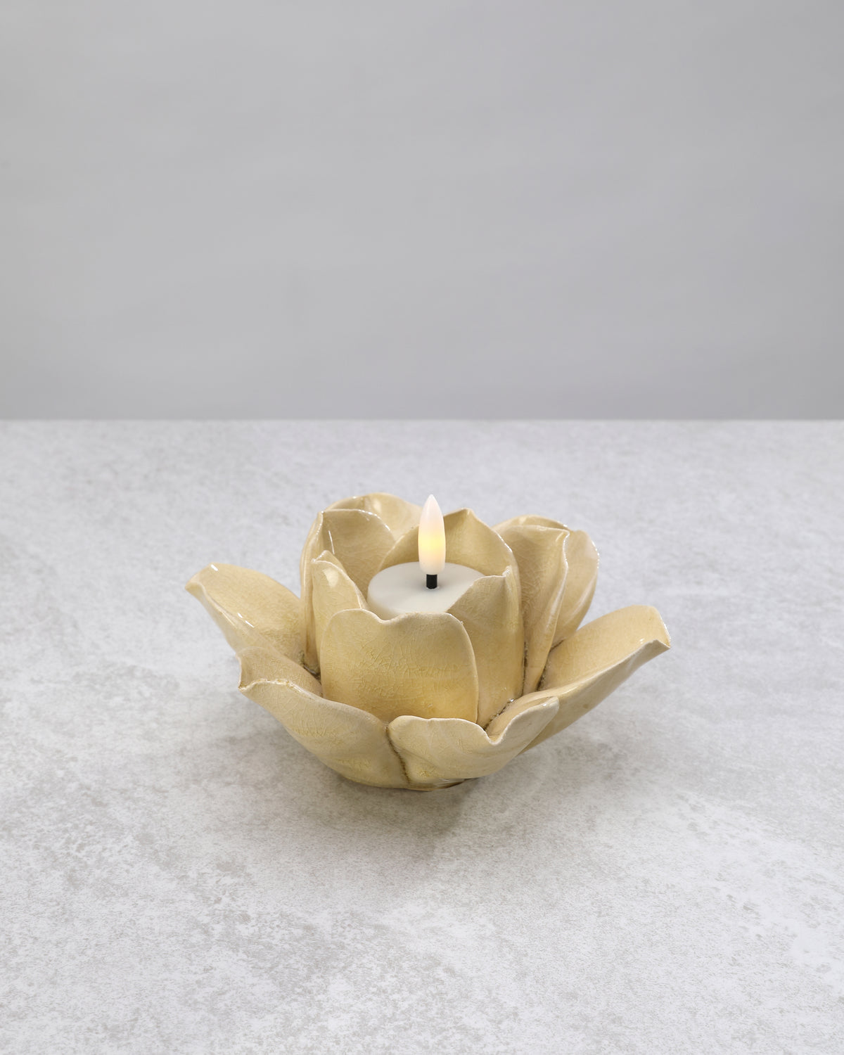 Soft gold ceramic lotus tea light holder with a lit candle