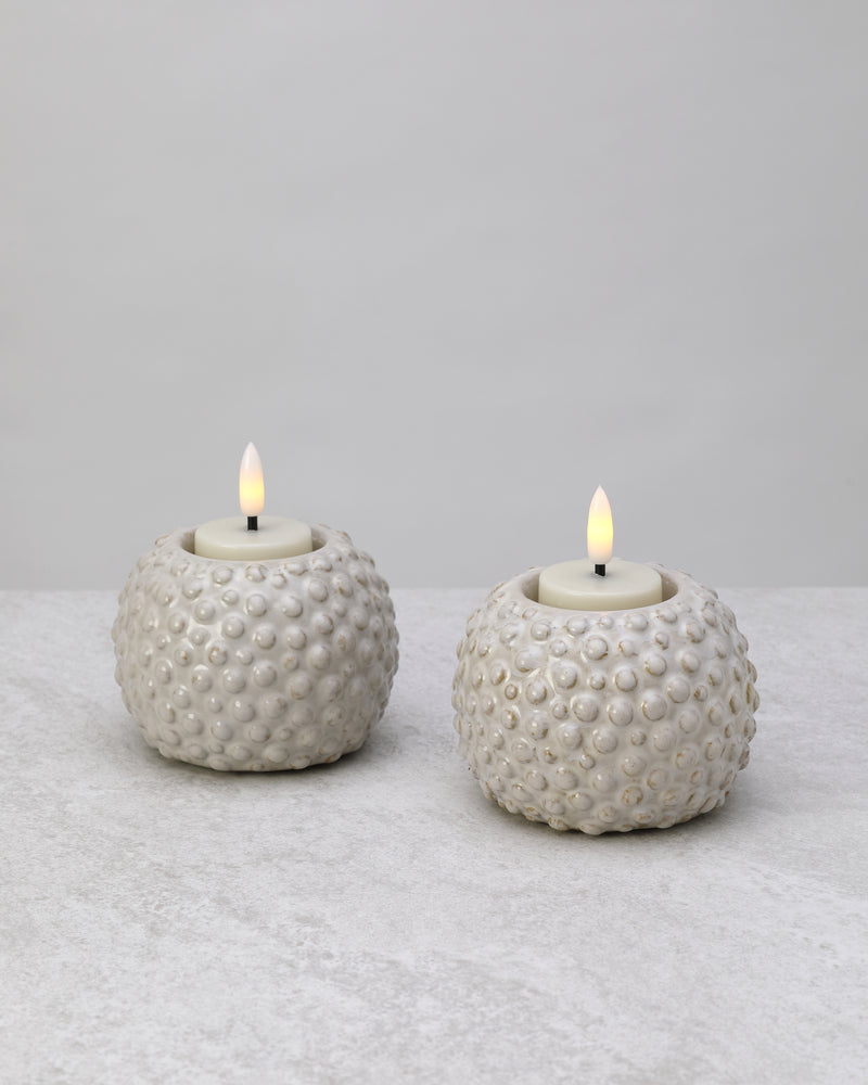 Pair of white textured glazed ceramic tea light holders with lit candles