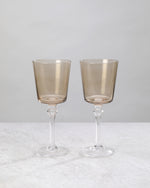 Two coffee-brown wine glasses on tall clear stems, on white