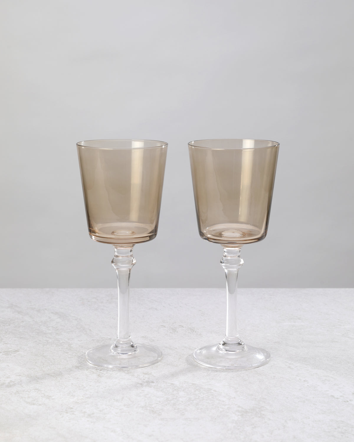 Two coffee-brown wine glasses on tall clear stems, on white