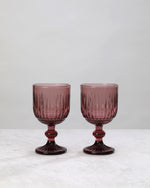 Pair of burgundy ribbed cut wine glasses on a white background