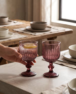 Burgundy ribbed wine glasses on a set table, a hand lifting one with a lemon slice