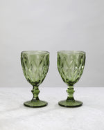 Two olive green diamond cut wine glasses on stems, on white