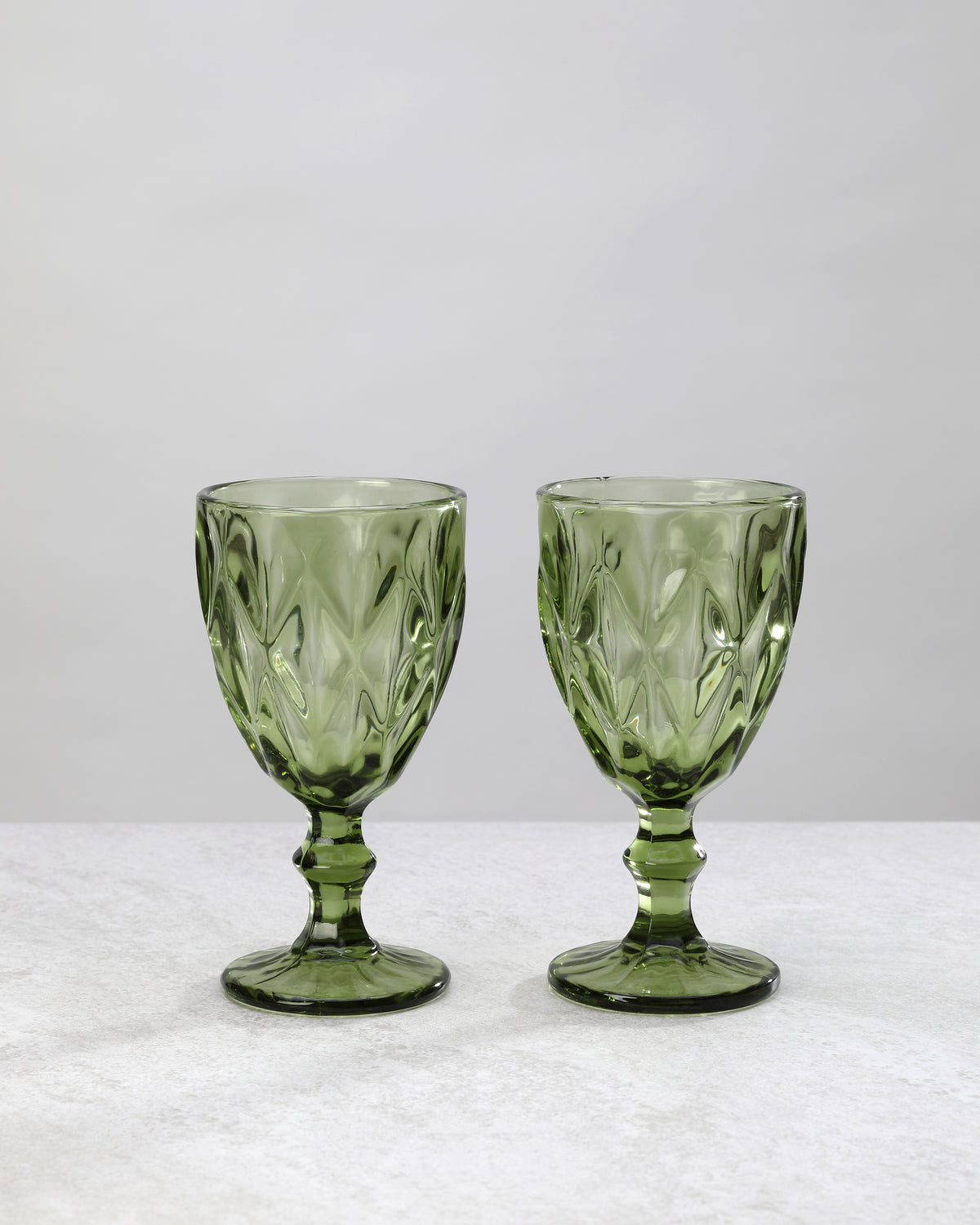 Two olive green diamond cut wine glasses on stems, on white