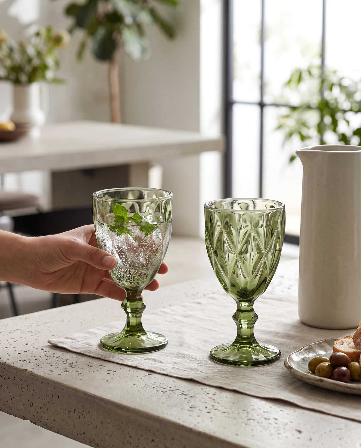 Olive diamond cut wine glasses with mint drinks on a table, a hand lifting one