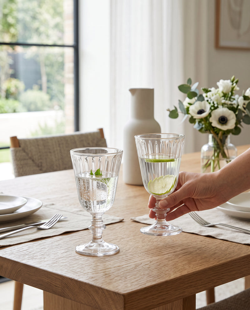 Clear ribbed wine glasses on a dining table with white anemones, a hand lifting one