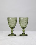 Two olive green small diamond wine glasses on stems, on white