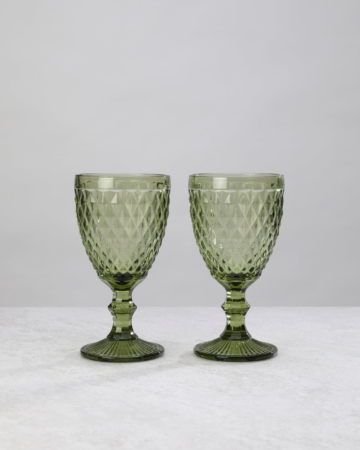 Two olive green small diamond wine glasses on stems, on white