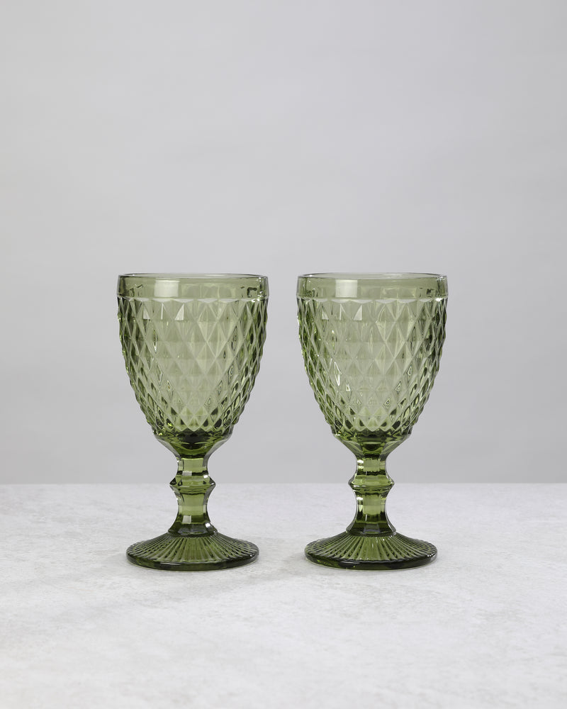 Two olive green small diamond wine glasses on stems, on white