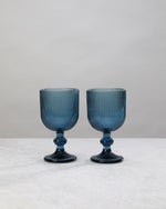 Two blue ribbed wine glasses on short knotted stems, on white